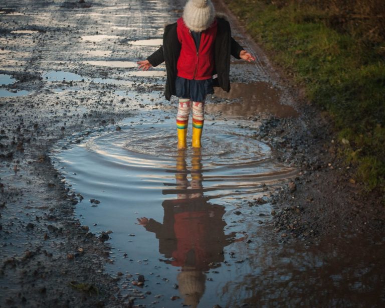 A young student standing in a giant puddle watching the ripples ripple out from where they are standing.